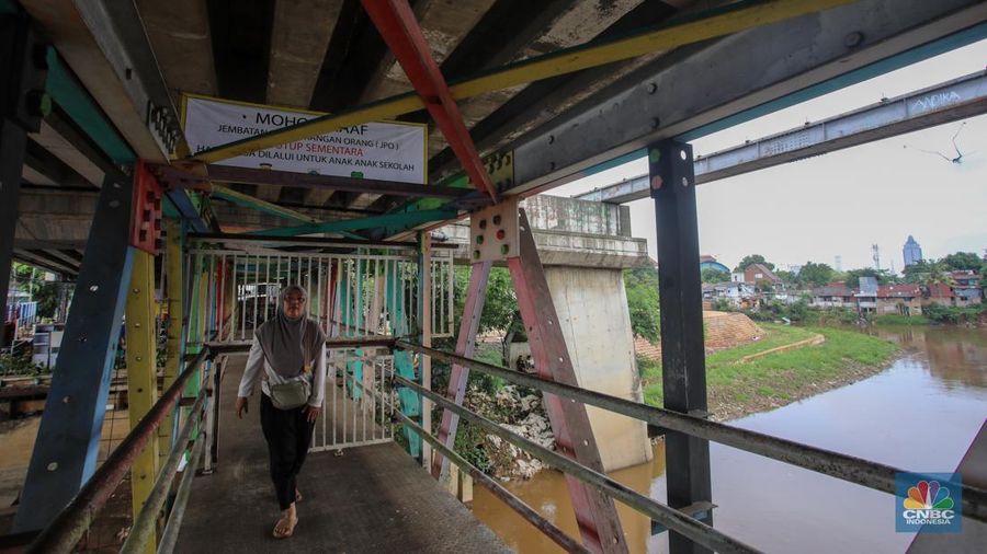 Warga melewati pintu kecil pada gerbang yang menutup akses jembatan penyeberangan orang (JPO) di kolong flyover Kalibata, Jakarta, Rabu (19/2/2025). (CNBC Indonesia/Martyasari Rizky)