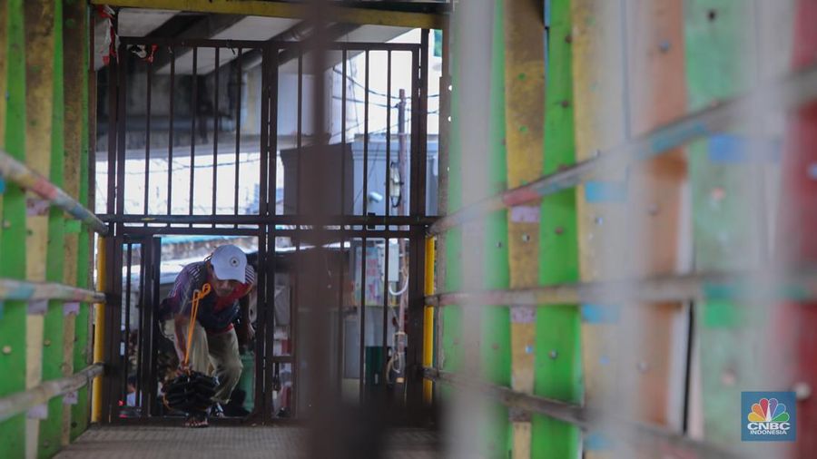 Warga melewati pintu kecil pada gerbang yang menutup akses jembatan penyeberangan orang (JPO) di kolong flyover Kalibata, Jakarta, Rabu (19/2/2025). (CNBC Indonesia/Martyasari Rizky)