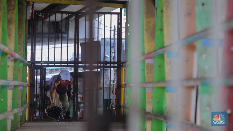 Warga melewati pintu kecil pada gerbang yang menutup akses jembatan penyeberangan orang (JPO) di kolong flyover Kalibata, Jakarta, Rabu (19/2/2025). (CNBC Indonesia/Martyasari Rizky)