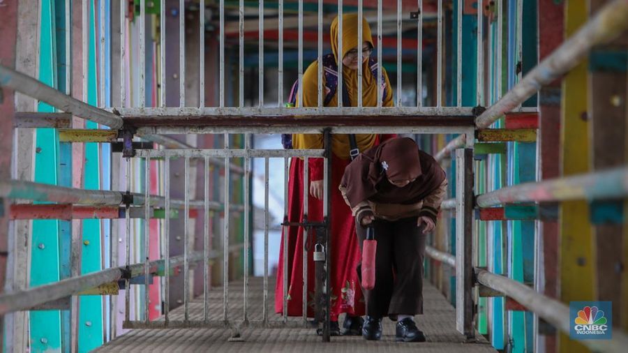 Warga melewati pintu kecil pada gerbang yang menutup akses jembatan penyeberangan orang (JPO) di kolong flyover Kalibata, Jakarta, Rabu (19/2/2025). (CNBC Indonesia/Martyasari Rizky)