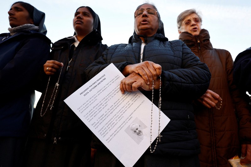 Orang-orang berkumpul untuk berdoa Rosario di patung mendiang Paus Yohanes Paulus II di luar Rumah Sakit Gemelli, tempat Paus Fransiskus dirawat, di Roma, Italia, 22 Februari 2025. (REUTERS/Vincenzo Livieri)