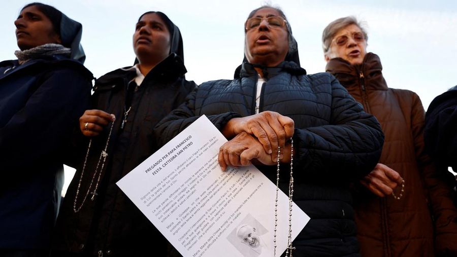 Orang-orang berkumpul untuk berdoa Rosario di patung mendiang Paus Yohanes Paulus II di luar Rumah Sakit Gemelli, tempat Paus Fransiskus dirawat, di Roma, Italia, 22 Februari 2025. (REUTERS/Vincenzo Livieri)