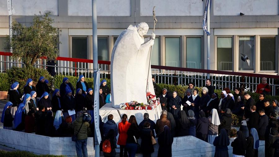 Orang-orang berkumpul untuk berdoa Rosario di patung mendiang Paus Yohanes Paulus II di luar Rumah Sakit Gemelli, tempat Paus Fransiskus dirawat, di Roma, Italia, 22 Februari 2025. (REUTERS/Vincenzo Livieri)