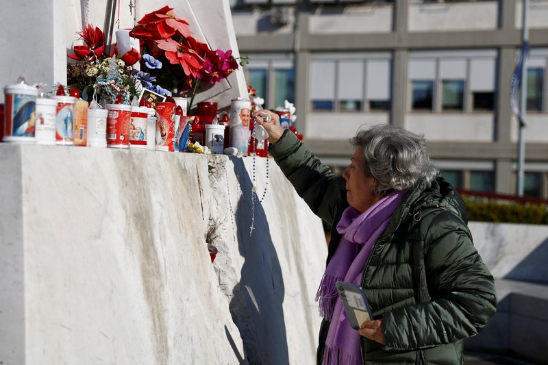Orang-orang berkumpul untuk berdoa Rosario di patung mendiang Paus Yohanes Paulus II di luar Rumah Sakit Gemelli, tempat Paus Fransiskus dirawat, di Roma, Italia, 22 Februari 2025. (REUTERS/Vincenzo Livieri)