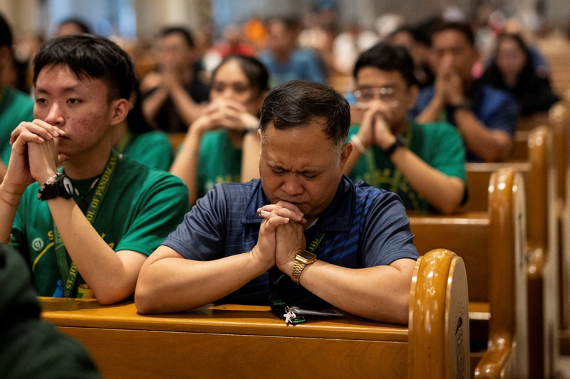 Orang-orang berkumpul untuk berdoa Rosario di patung mendiang Paus Yohanes Paulus II di luar Rumah Sakit Gemelli, tempat Paus Fransiskus dirawat, di Roma, Italia, 22 Februari 2025. (REUTERS/Vincenzo Livieri)