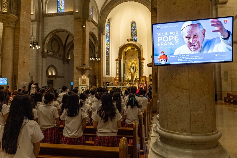 Orang-orang berkumpul untuk berdoa Rosario di patung mendiang Paus Yohanes Paulus II di luar Rumah Sakit Gemelli, tempat Paus Fransiskus dirawat, di Roma, Italia, 22 Februari 2025. (REUTERS/Vincenzo Livieri)