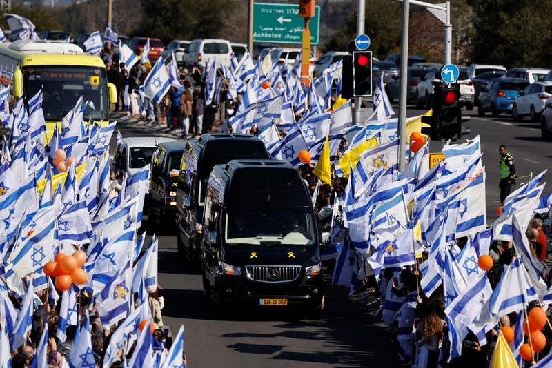 Warga Israel mengibarkan bendera Israel saat konvoi yang membawa peti jenazah Shiri, 32 tahun, dan kedua anaknya Kfir, 9 bulan, dan Ariel, 4 tahun, dari keluarga Bibas, yang diculik dari rumah mereka di Kibbutz Nir Oz selama serangan mematikan pada 7 Oktober 2023 oleh Hamas dan kemudian dibunuh di Gaza, berjalan sebagai bagian dari prosesi pemakaman mereka di Ashkelon, Israel, 26 Februari 2025. (REUTERS/Amir Cohen)
