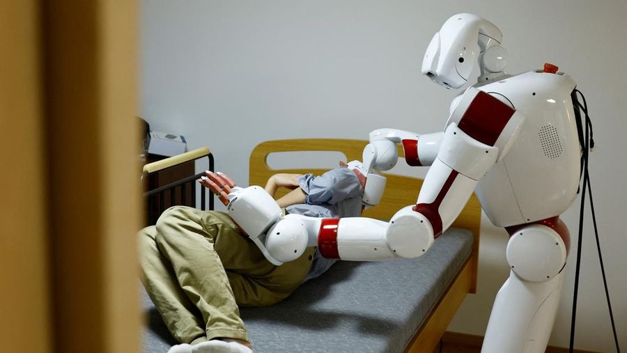 AIREC, robot humanoid nan digerakkan oleh kepintaran buatan (AI), mendemonstrasikan manuver untuk mengganti popok alias mencegah luka baring dengan seorang peneliti di laboratorium Universitas Waseda di Tokyo, Jepang. (REUTERS/Kim Kyung-Hoon)