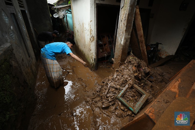 Warga membersihkan sisa-sisa lumpur dan sampah banjir yang melanda Kampung Pensiunan, Desa Tugu Selatan, Kecamatan Cisarua, Kabupaten Bogor, Jawa Barat, Senin (3/3/2025). (CNBC Indonesia/Tri Susilo)