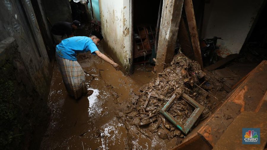 Warga membersihkan sisa-sisa lumpur dan sampah banjir yang melanda Kampung Pensiunan, Desa Tugu Selatan, Kecamatan Cisarua, Kabupaten Bogor, Jawa Barat, Senin (3/3/2025). (CNBC Indonesia/Tri Susilo)