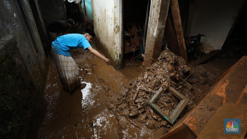 Warga membersihkan sisa-sisa lumpur dan sampah banjir yang melanda Kampung Pensiunan, Desa Tugu Selatan, Kecamatan Cisarua, Kabupaten Bogor, Jawa Barat, Senin (3/3/2025). (CNBC Indonesia/Tri Susilo)
