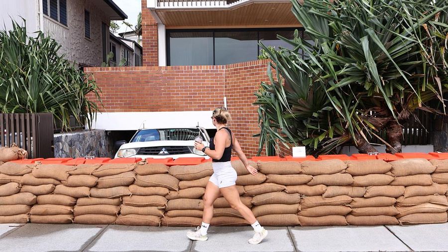 Seorang wanita berjalan melewati karung pasir yang didirikan di luar sebuah rumah untuk mencegah banjir sebelum Siklon Alfred menerjang daratan, di Currumbin di Gold Coast, Australia, 6 Maret 2025. (AAP Image/Jason O'Brien/via REUTERS)