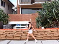 Seorang wanita berjalan melewati karung pasir yang didirikan di luar sebuah rumah untuk mencegah banjir sebelum Siklon Alfred menerjang daratan, di Currumbin di Gold Coast, Australia, 6 Maret 2025. (AAP Image/Jason O'Brien/via REUTERS)
