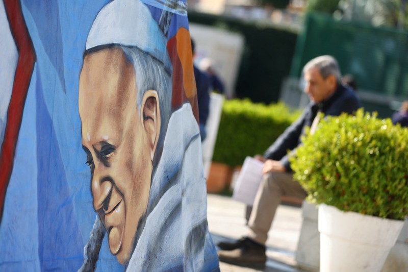 Orang-orang berdoa di dekat patung mendiang Paus Yohanes Paulus II di luar Rumah Sakit Gemelli tempat Paus Fransiskus dirawat, di Roma, Italia, 5 Maret 2025. (REUTERS/Remo Casilli)