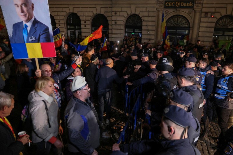 Pendukung kandidat sayap kanan Calin Georgescu berhadapan dengan polisi anti huru hara di luar biro pemilihan pusat Rumania, setelah penolakan pencalonannya untuk pemilihan ulang presiden pada bulan Mei, di Bukares, Rumania, 9 Maret 2025. Pendukung kandidat sayap kanan Calin Georgescu berhadapan dengan polisi anti huru hara di luar biro pemilihan pusat Rumania, setelah penolakan pencalonannya untuk pemilihan ulang presiden pada bulan Mei, di Bukares, Rumania, 9 Maret 2025. (Inquam Photos/George Calin via REUTERS)