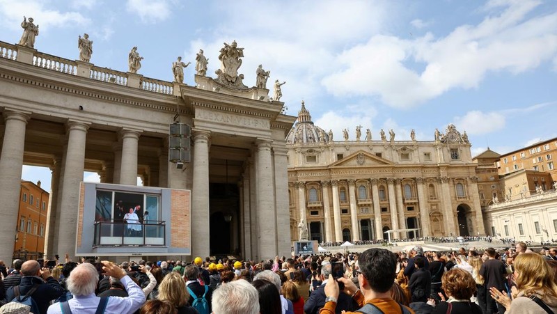 Orang-orang menonton Paus Fransiskus selama penampilan publik pertamanya dalam lima minggu, di layar lebar di Lapangan Santo Petrus, di Vatikan, 23 Maret 2025. (REUTERS/Matteo Minnella)