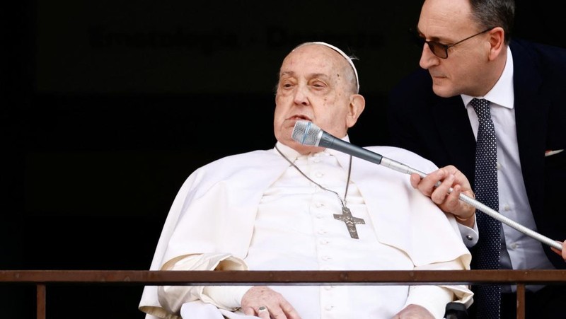 Orang-orang menonton Paus Fransiskus selama penampilan publik pertamanya dalam lima minggu, di layar lebar di Lapangan Santo Petrus, di Vatikan, 23 Maret 2025. (REUTERS/Matteo Minnella)