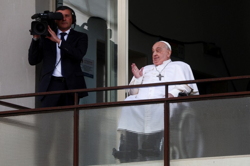 Orang-orang menonton Paus Fransiskus selama penampilan publik pertamanya dalam lima minggu, di layar lebar di Lapangan Santo Petrus, di Vatikan, 23 Maret 2025. (REUTERS/Matteo Minnella)