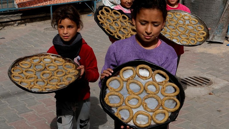 Perempuan Palestina yang mengungsi menyiapkan penganan tradisional untuk hari raya Idul Fitri yang menandai berakhirnya bulan puasa Ramadan, di Khan Younis di Jalur Gaza selatan pada 29 Maret 2025. (REUTERS/Hatem Khaled)