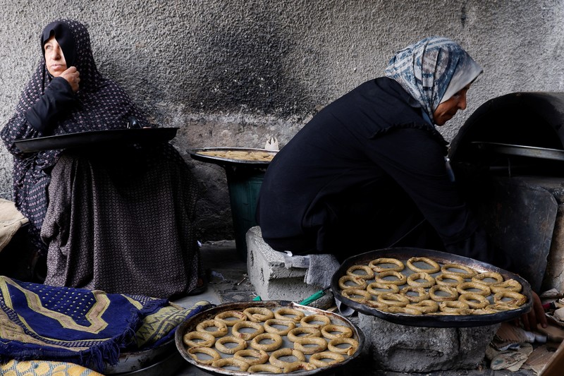 Perempuan Palestina yang mengungsi menyiapkan penganan tradisional untuk hari raya Idul Fitri yang menandai berakhirnya bulan puasa Ramadan, di Khan Younis di Jalur Gaza selatan pada 29 Maret 2025. (REUTERS/Hatem Khaled)