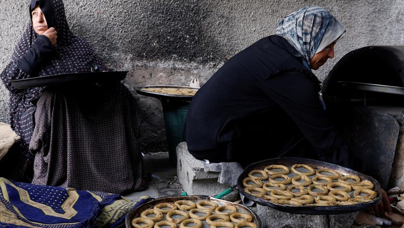 Perempuan Palestina yang mengungsi menyiapkan penganan tradisional untuk hari raya Idul Fitri yang menandai berakhirnya bulan puasa Ramadan, di Khan Younis di Jalur Gaza selatan pada 29 Maret 2025. (REUTERS/Hatem Khaled)