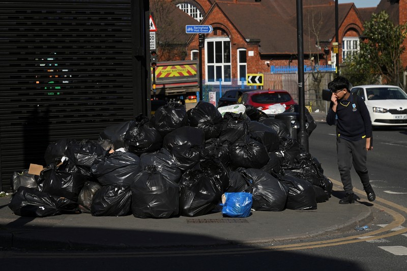 Seorang anak sekolah menutup hidungnya karena mencium bau tumpukan sampah yang menghalangi trotoar, saat aksi mogok pekerja tempat sampah Birmingham yang diwakili oleh serikat pekerja Unite memasuki minggu keempat, di Sparkhill, Birmingham, Inggris, 2 April 2025. (REUTERS/Jaimi Joy)