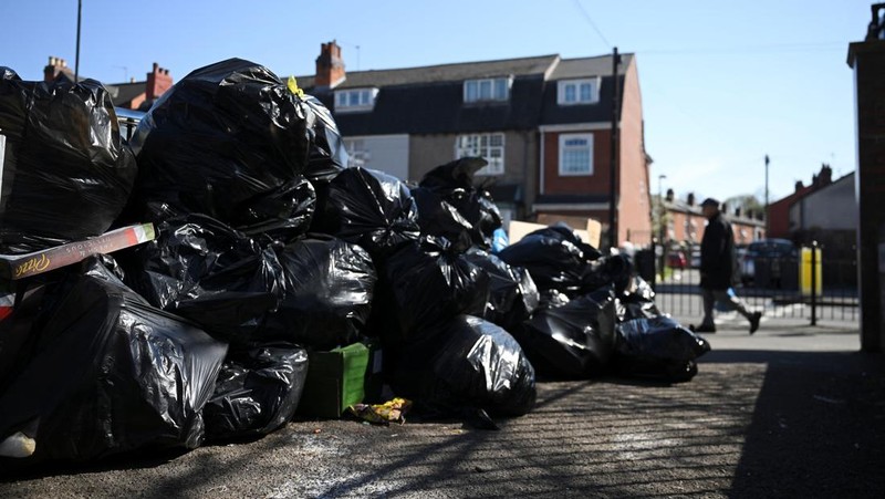 Seorang anak sekolah menutup hidungnya karena mencium bau tumpukan sampah yang menghalangi trotoar, saat aksi mogok pekerja tempat sampah Birmingham yang diwakili oleh serikat pekerja Unite memasuki minggu keempat, di Sparkhill, Birmingham, Inggris, 2 April 2025. (REUTERS/Jaimi Joy)