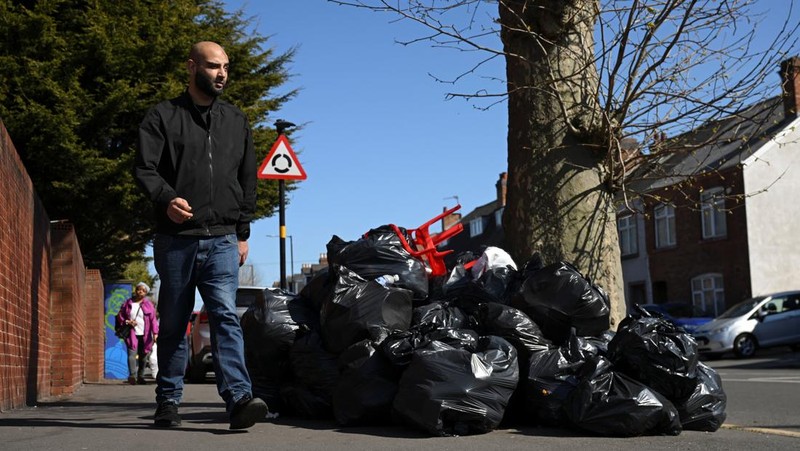 Seorang anak sekolah menutup hidungnya karena mencium bau tumpukan sampah yang menghalangi trotoar, saat aksi mogok pekerja tempat sampah Birmingham yang diwakili oleh serikat pekerja Unite memasuki minggu keempat, di Sparkhill, Birmingham, Inggris, 2 April 2025. (REUTERS/Jaimi Joy)