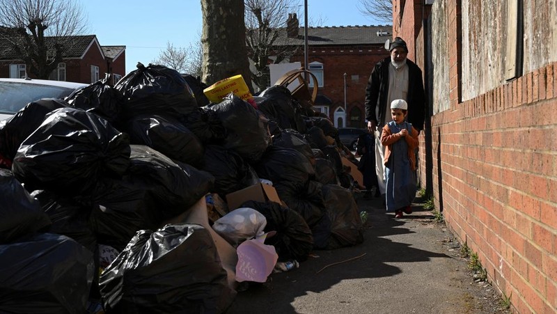 Seorang anak sekolah menutup hidungnya karena mencium bau tumpukan sampah yang menghalangi trotoar, saat aksi mogok pekerja tempat sampah Birmingham yang diwakili oleh serikat pekerja Unite memasuki minggu keempat, di Sparkhill, Birmingham, Inggris, 2 April 2025. (REUTERS/Jaimi Joy)