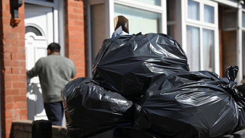 Seorang anak sekolah menutup hidungnya karena mencium bau tumpukan sampah yang menghalangi trotoar, saat aksi mogok pekerja tempat sampah Birmingham yang diwakili oleh serikat pekerja Unite memasuki minggu keempat, di Sparkhill, Birmingham, Inggris, 2 April 2025. (REUTERS/Jaimi Joy)