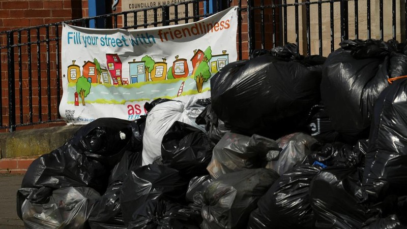 Seorang anak sekolah menutup hidungnya karena mencium bau tumpukan sampah yang menghalangi trotoar, saat aksi mogok pekerja tempat sampah Birmingham yang diwakili oleh serikat pekerja Unite memasuki minggu keempat, di Sparkhill, Birmingham, Inggris, 2 April 2025. (REUTERS/Jaimi Joy)
