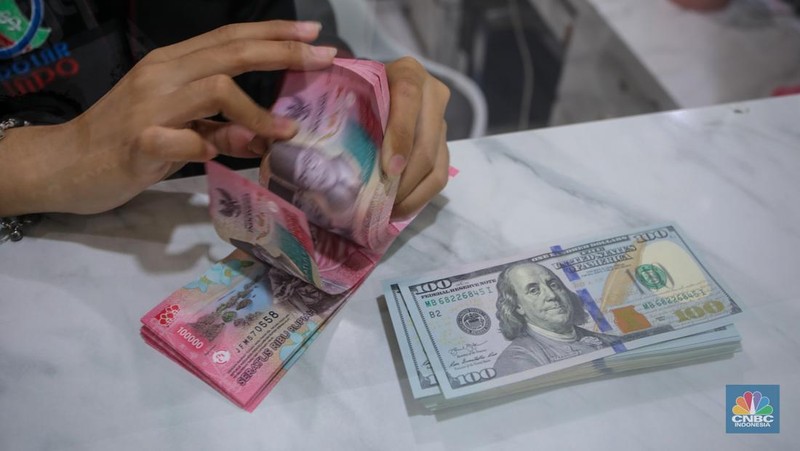 Petugas menjunjukkan uang pecahan dolar AS dan rupiah di Dolarindo Money Changer, Jakarta, Selasa (8/4/2025). (CNBC Indonesia/Faisal Rahman)