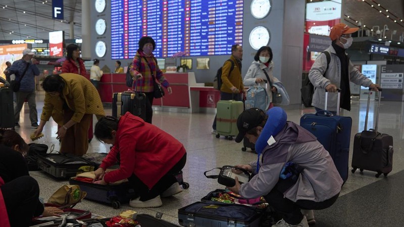 A traveller walks past by a board showing flights that are cancelled at the Capital International Airport Terminal 3 following gale wind alerts in Beijing, China, Saturday, April 12, 2025. (AP Photo/Ng Han Guan)