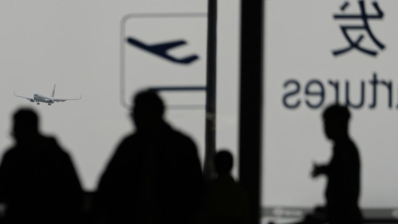A traveller walks past by a board showing flights that are cancelled at the Capital International Airport Terminal 3 following gale wind alerts in Beijing, China, Saturday, April 12, 2025. (AP Photo/Ng Han Guan)