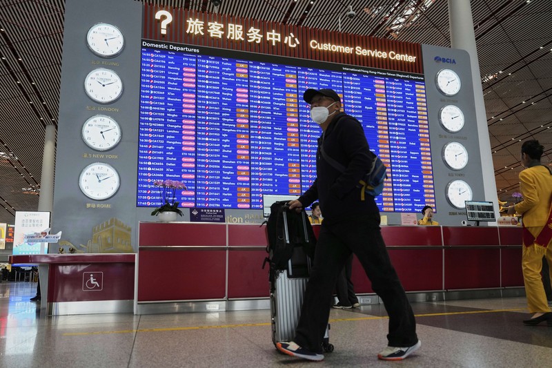 A traveller walks past by a board showing flights that are cancelled at the Capital International Airport Terminal 3 following gale wind alerts in Beijing, China, Saturday, April 12, 2025. (AP Photo/Ng Han Guan)