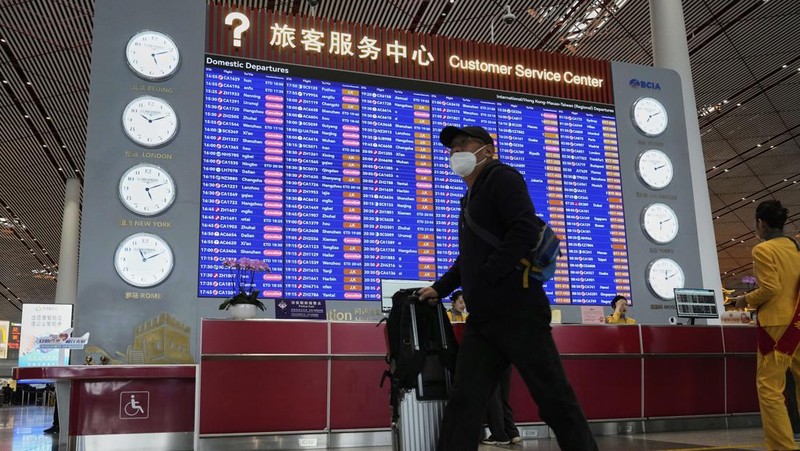 A traveller walks past by a board showing flights that are cancelled at the Capital International Airport Terminal 3 following gale wind alerts in Beijing, China, Saturday, April 12, 2025. (AP Photo/Ng Han Guan)