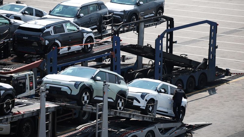 Sebuah pengangkut mobil yang mengangkut kendaraan buatan Kia Motors, yang merupakan bagian dari perusahaan pembuat mobil terbesar Korea Selatan, Hyundai Motor, melintasi pohon sakura yang sedang berbunga di dekat pelabuhan Pyeongtaek di Pyeongtaek, Korea Selatan, Selasa (15/4/2024). (REUTERS/Kim Hong-Ji)