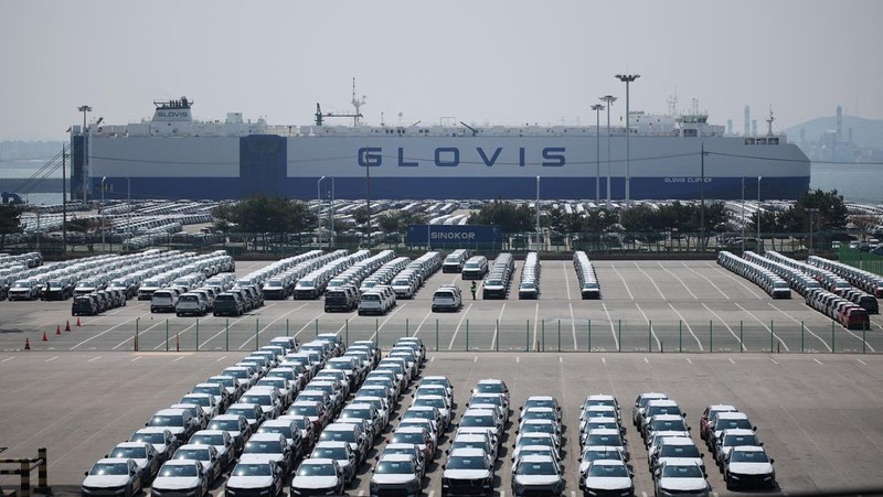 Sebuah pengangkut mobil yang mengangkut kendaraan buatan Kia Motors, yang merupakan bagian dari perusahaan pembuat mobil terbesar Korea Selatan, Hyundai Motor, melintasi pohon sakura yang sedang berbunga di dekat pelabuhan Pyeongtaek di Pyeongtaek, Korea Selatan, Selasa (15/4/2024). (REUTERS/Kim Hong-Ji)