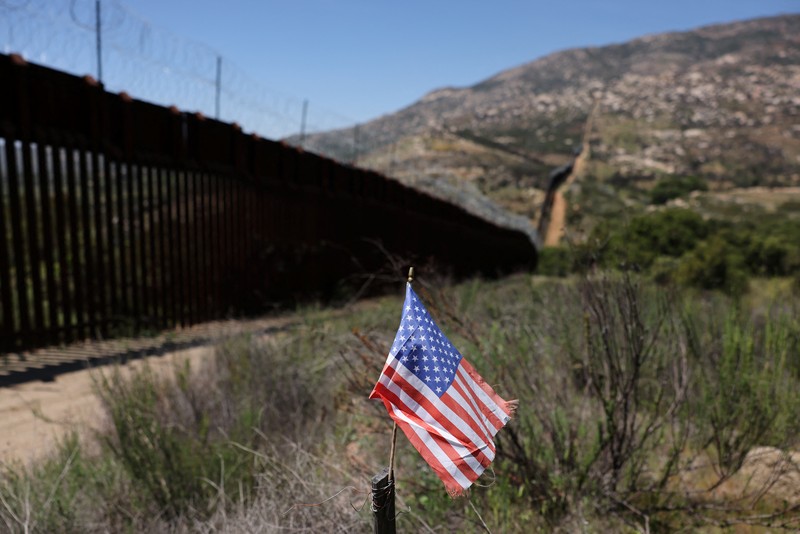 Bendera AS berdiri di tiang di samping tembok perbatasan di perbatasan Meksiko dan AS di Campo, California, AS, 20 April 2025. (REUTERS/David Swanson)