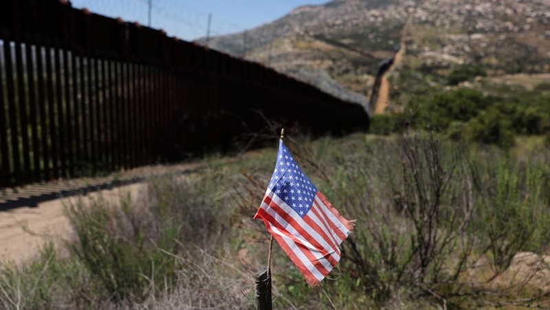 Bendera AS berdiri di tiang di samping tembok perbatasan di perbatasan Meksiko dan AS di Campo, California, AS, 20 April 2025. (REUTERS/David Swanson)