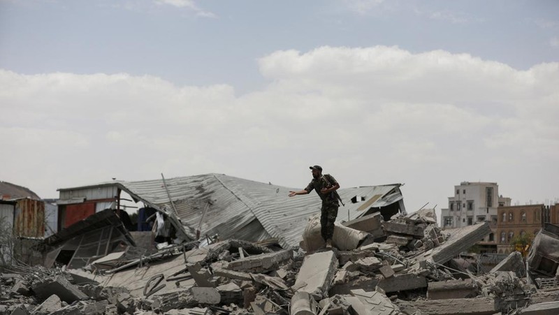 Warga berdiri pada di dekat mobil yang rusak pada lokasi serangan udara AS di Sanaa, Yaman, Minggu (27/4/2025). (REUTERS/Khaled Abdullah)