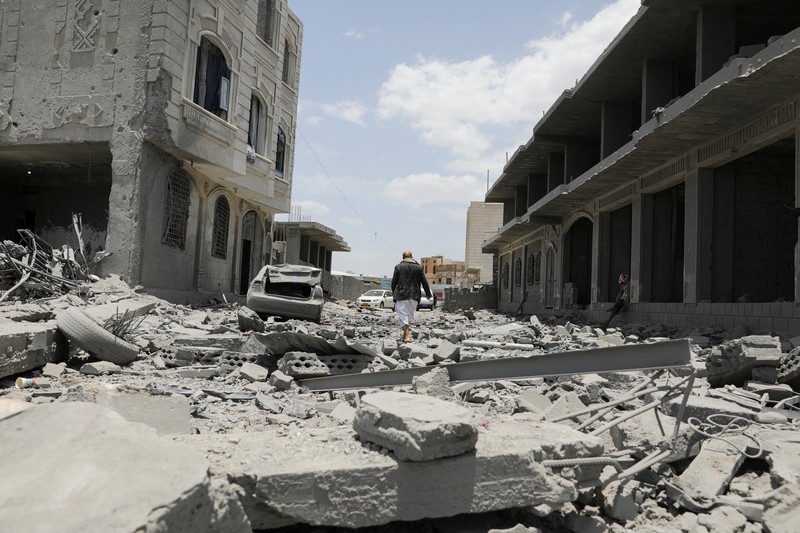 Warga berdiri pada di dekat mobil yang rusak pada lokasi serangan udara AS di Sanaa, Yaman, Minggu (27/4/2025). (REUTERS/Khaled Abdullah)