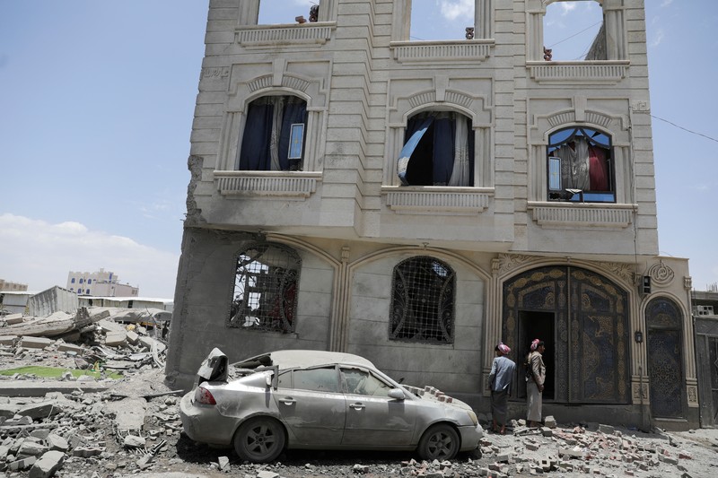 Warga berdiri pada di dekat mobil yang rusak pada lokasi serangan udara AS di Sanaa, Yaman, Minggu (27/4/2025). (REUTERS/Khaled Abdullah)