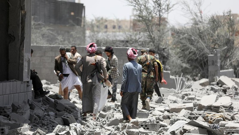 Warga berdiri pada di dekat mobil yang rusak pada lokasi serangan udara AS di Sanaa, Yaman, Minggu (27/4/2025). (REUTERS/Khaled Abdullah)