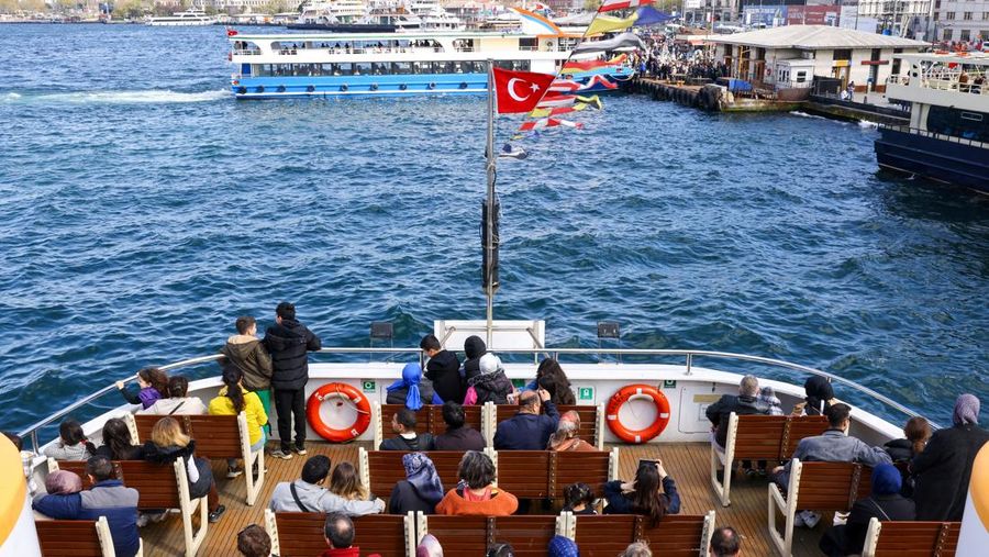 Orang-orang memberi makan burung camar saat mereka berlayar melalui Bosphorus dengan feri di Istanbul, Turki, 23 April 2025. (REUTERS/Umit Bektas)