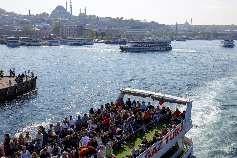 Orang-orang memberi makan burung camar saat mereka berlayar melalui Bosphorus dengan feri di Istanbul, Turki, 23 April 2025. (REUTERS/Umit Bektas)
