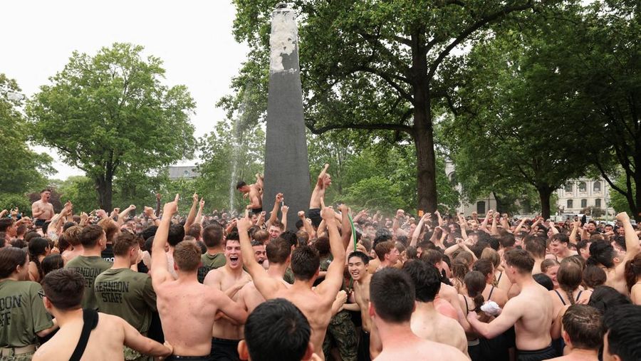 Para anggota Plebe berlomba untuk memulai tugas mereka membentuk piramida manusia untuk memanjat Monumen Herndon, sebuah obelisk granit setinggi 21 kaki, yang dilapisi dengan lapisan tebal lemak nabati, dalam ritual tahunan yang menandai selesainya kelas tahun pertama di Akademi Angkatan Laut AS di Annapolis, Maryland, AS, 14 Mei 2025. (REUTERS/Kevin Lamarque)