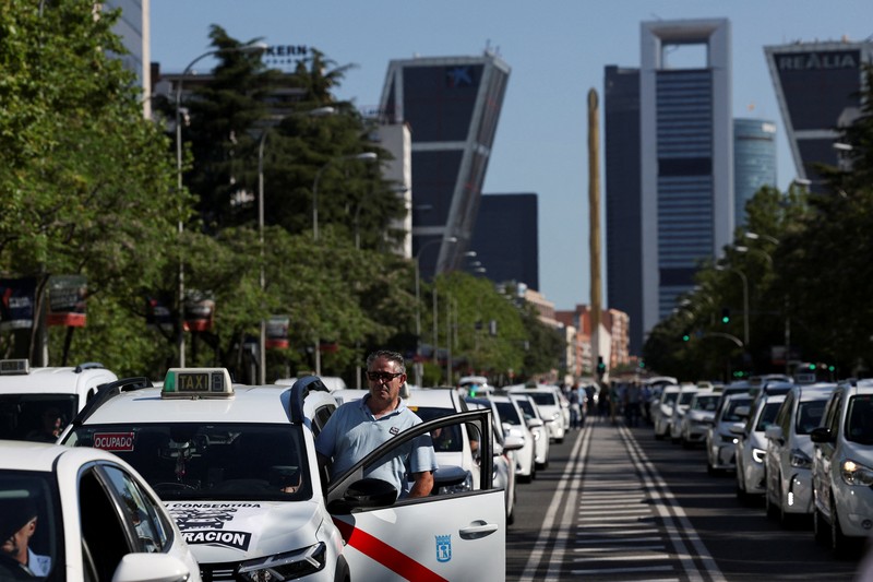 People cross a street as taxi drivers take part in a protest march against ride-hailing vehicles, in Madrid, Spain, May 28, 2025. REUTERS/Violeta Santos Moura
