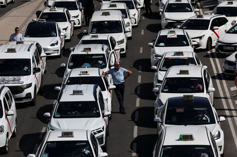 SPAIN-PROTEST/TAXI People cross a street as taxi drivers take part in a protest march against ride-hailing vehicles, in Madrid, Spain, May 28, 2025. REUTERS/Violeta Santos Moura
