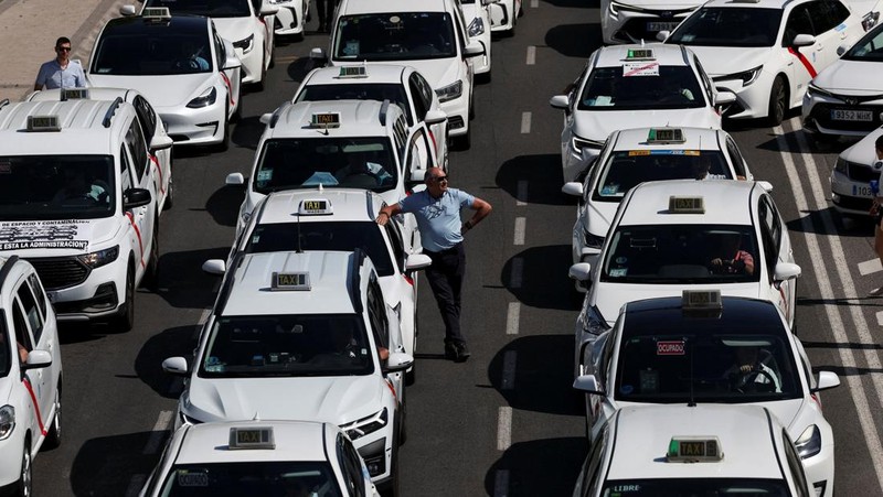 People cross a street as taxi drivers take part in a protest march against ride-hailing vehicles, in Madrid, Spain, May 28, 2025. REUTERS/Violeta Santos Moura
